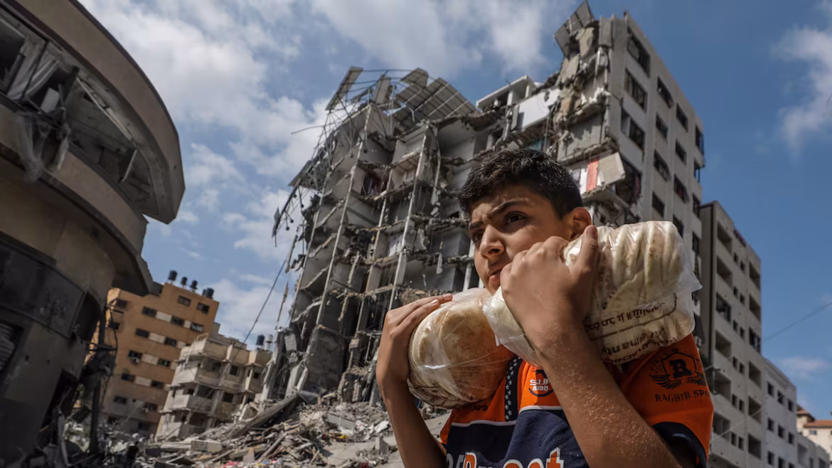 Un niño palestino lleva un pan entre edificios destruidos por los bombardeos israelíes en la ciudad de Gaza. Foto: MOHAMMED SABER (EFE/EPA)